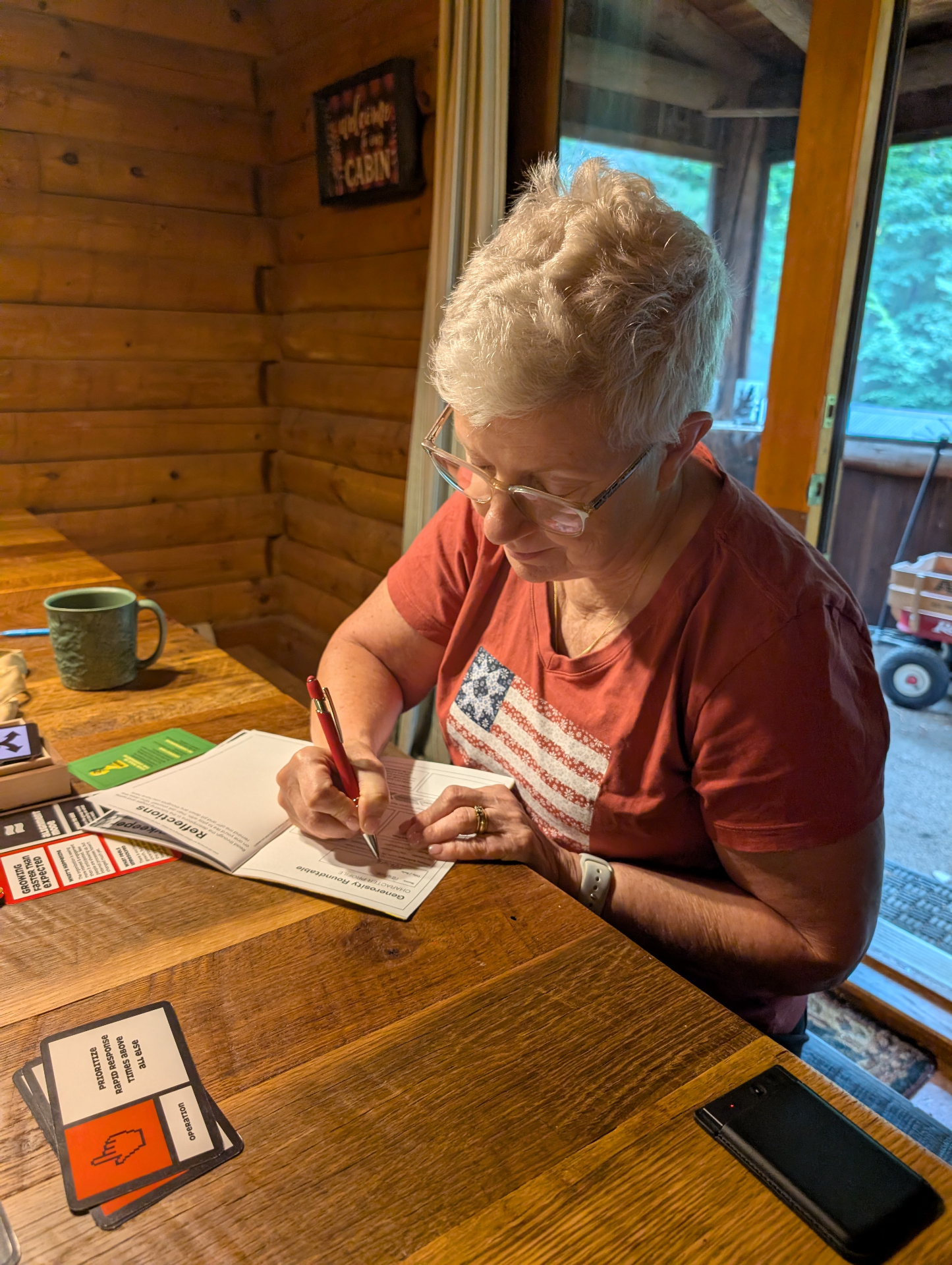 Pauline sitting at a cabin table, filling in her character profile in pen with a mug of coffee beside her.